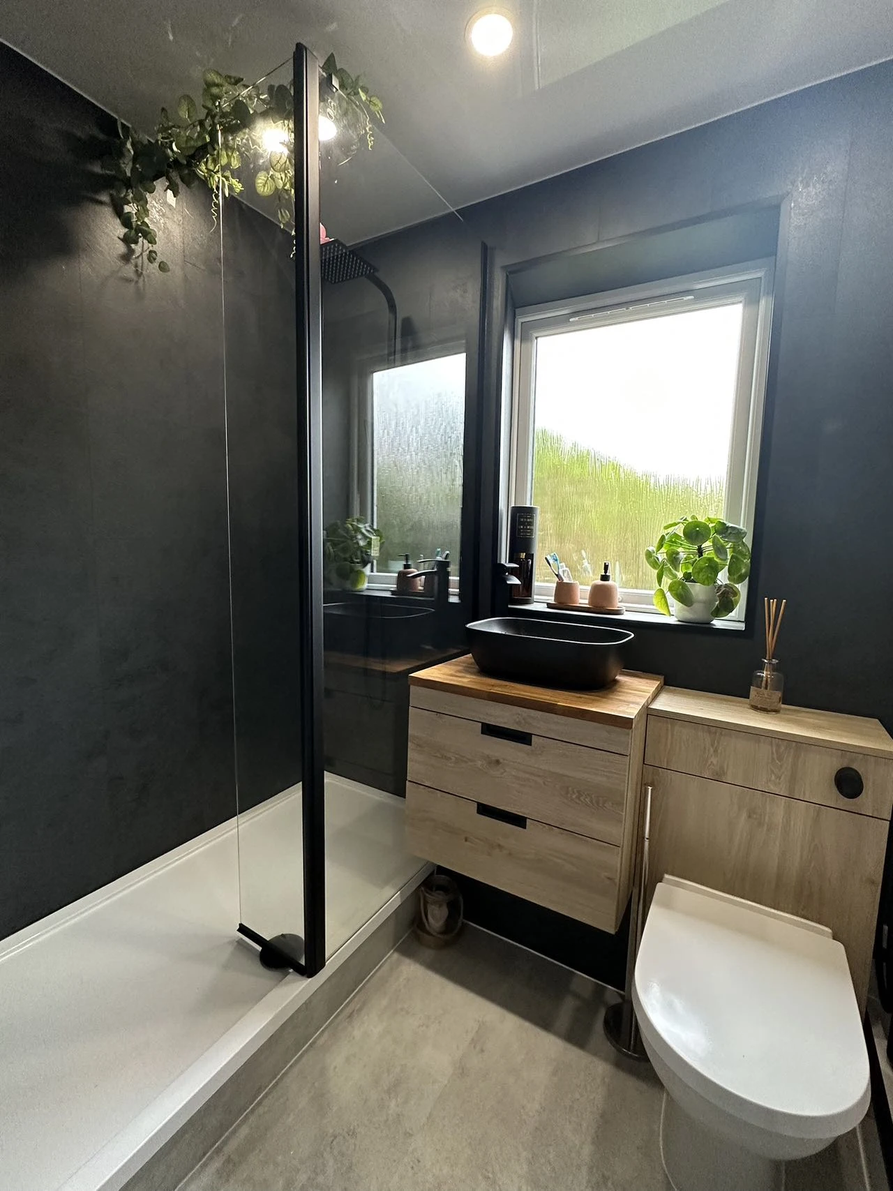 Warm oak-effect vanity against charcoal walls beside a walk-in shower