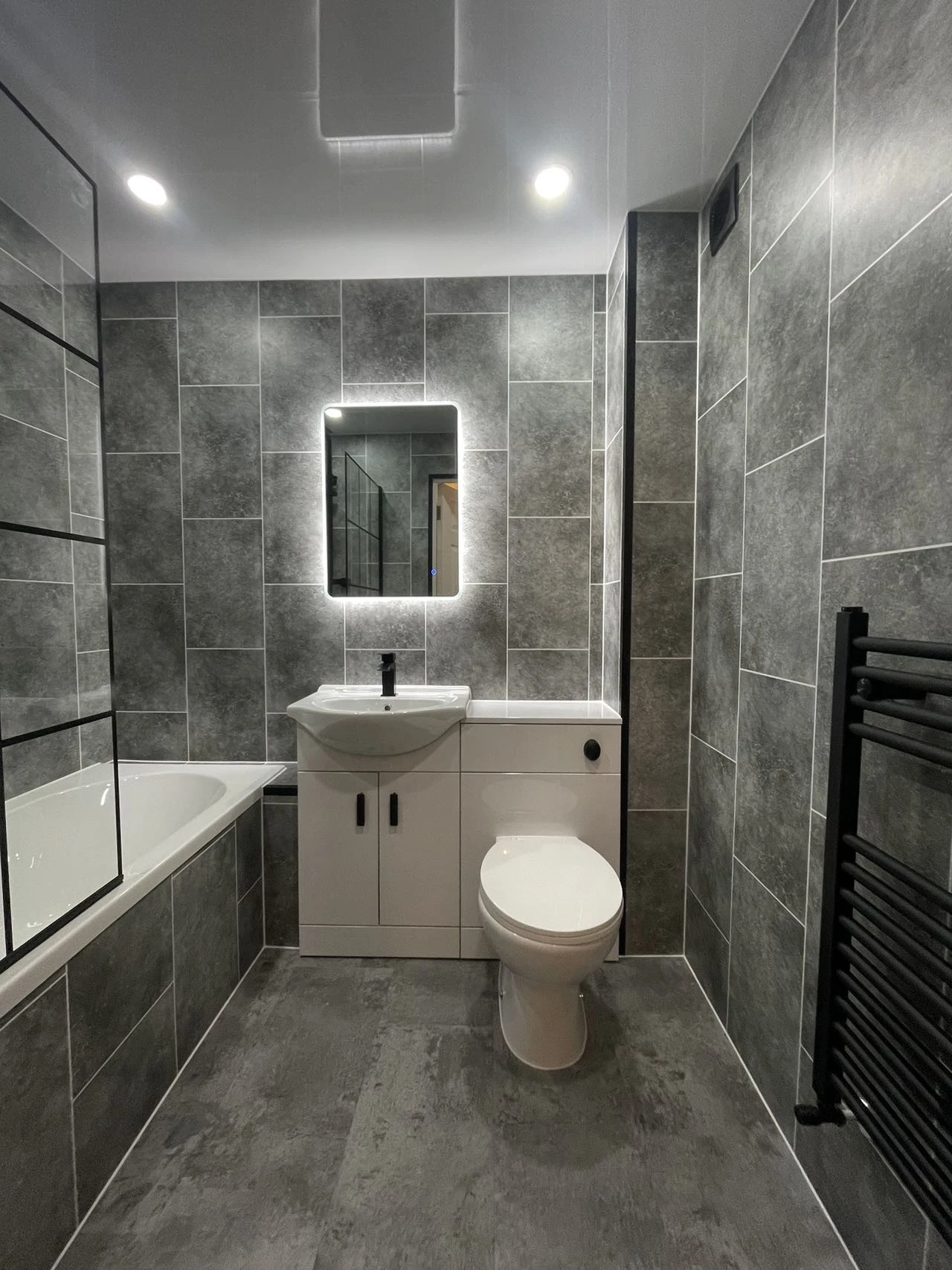 Contemporary grey bathroom with a bath, white vanity and illuminated mirror