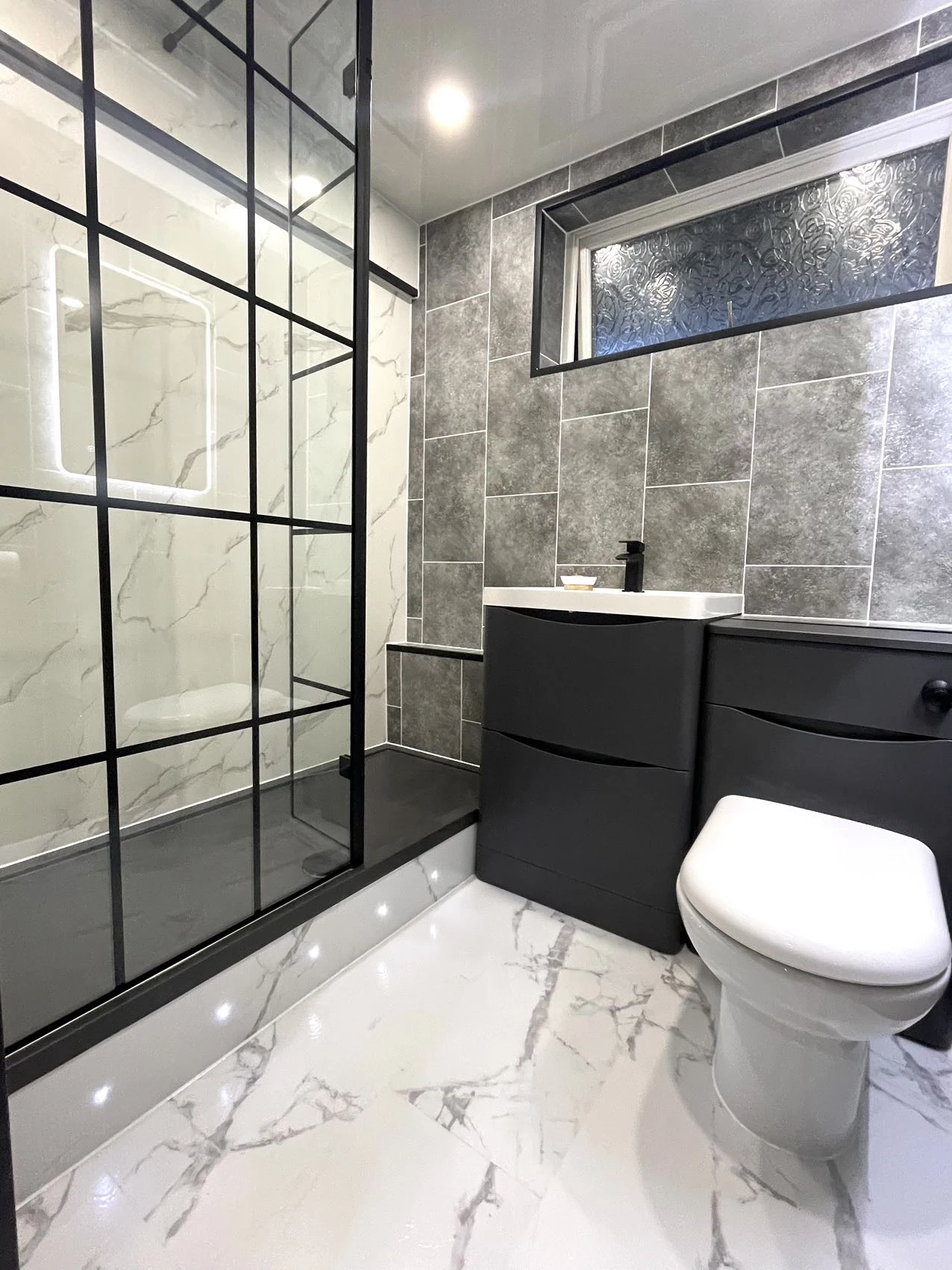 White marble-effect bathroom with black-framed shower glass and dark vanity furniture