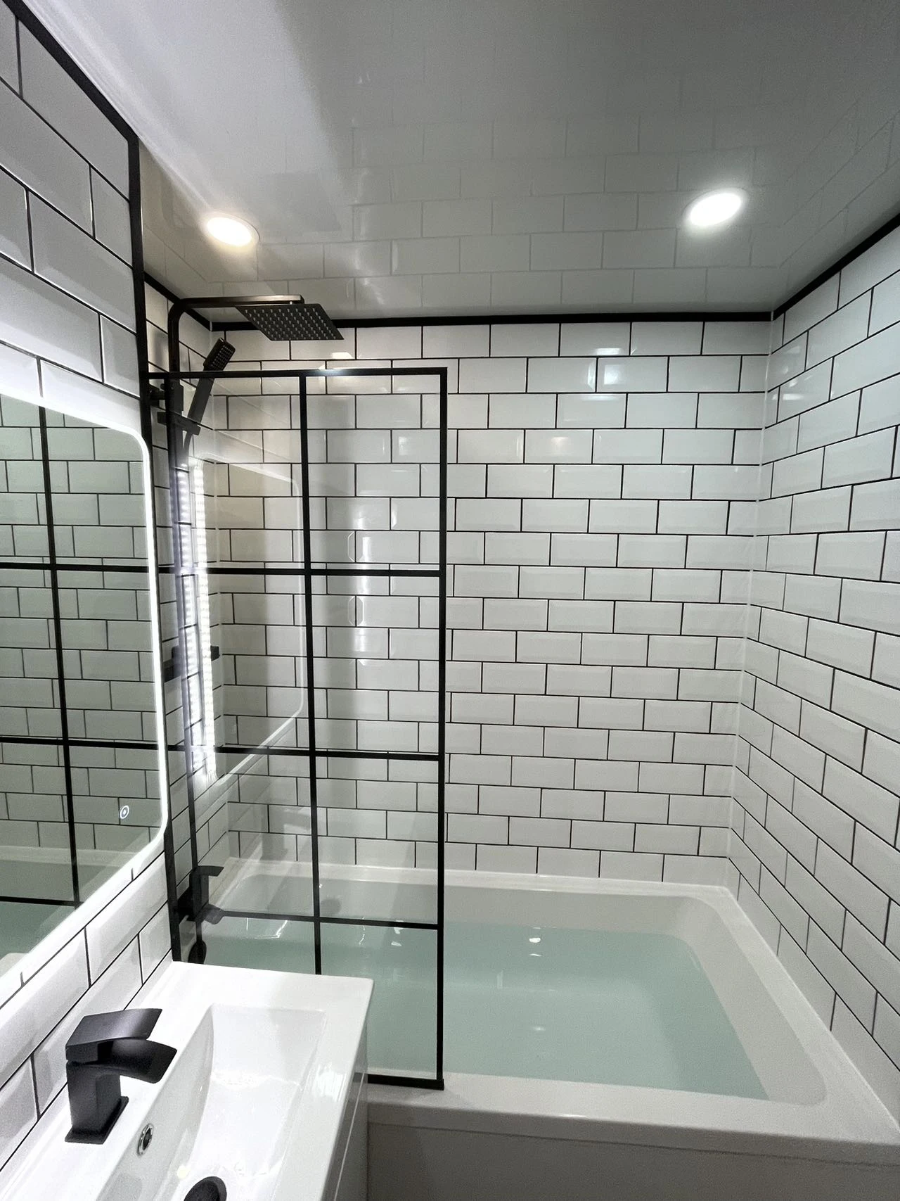 Finished bathroom with white tile-effect walls, bath and black-framed screen