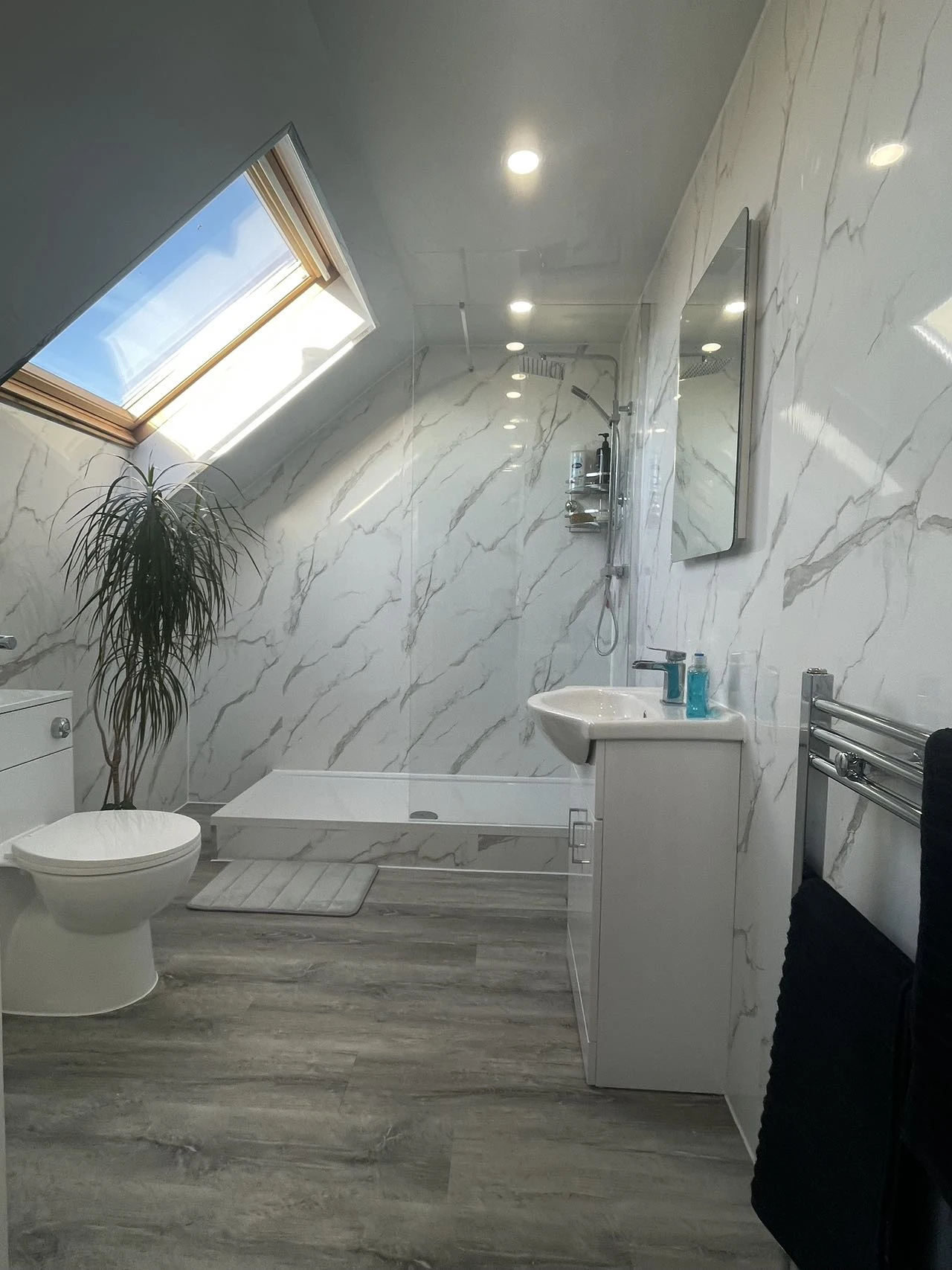 Bright loft bathroom with a skylight and marble-effect shower walls