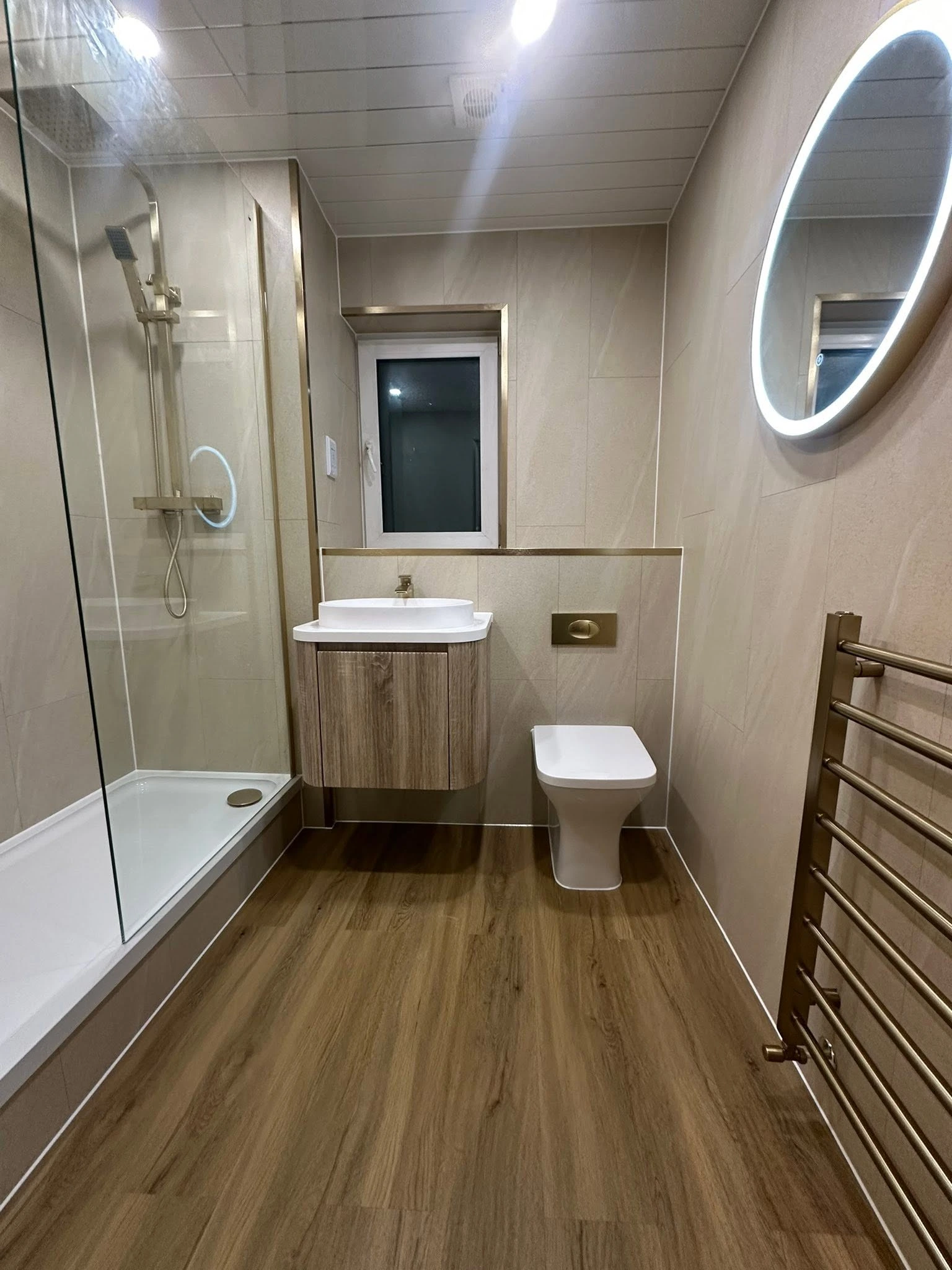 Completed warm neutral shower room with wood-effect flooring, floating vanity and brass fittings